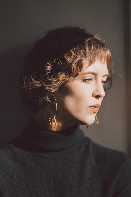 Young contemplative female in black outfit with wavy brown hair looking away on gray background