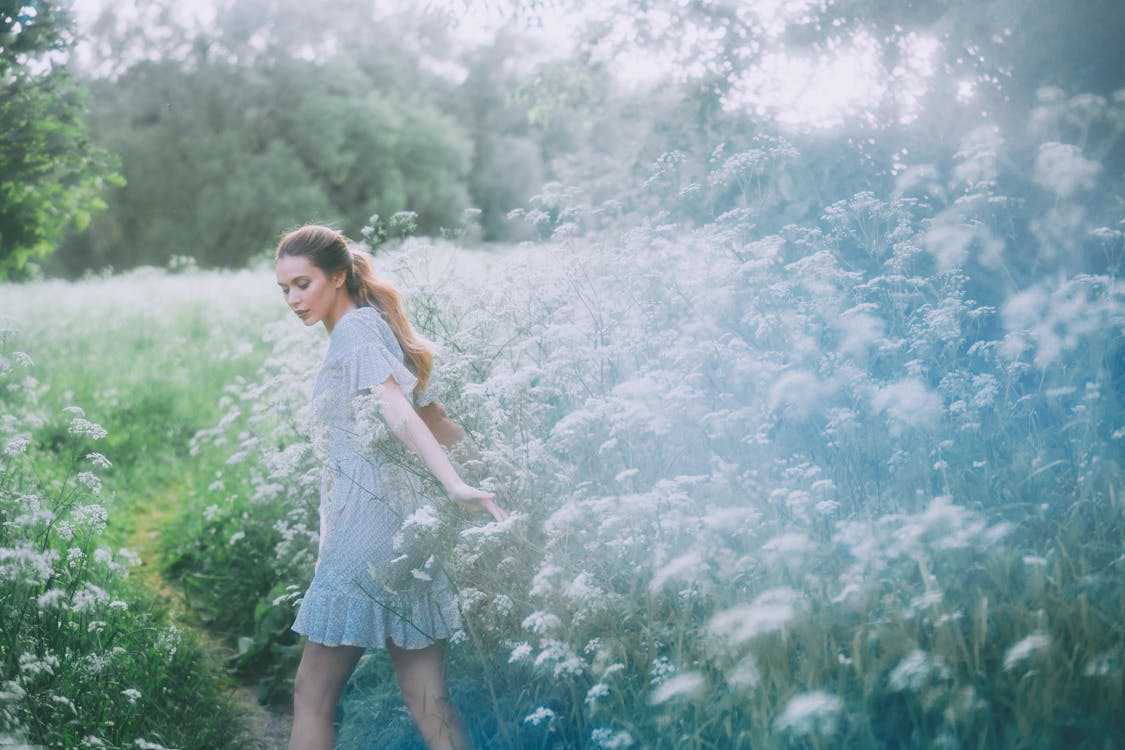 Gentle woman walking on path in field with blooming flowers