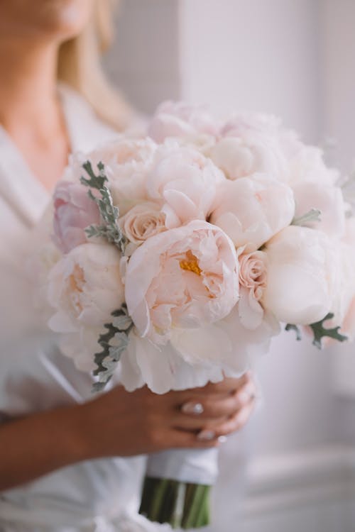 Crop anonymous woman holding blossoming bridal bouquet with pleasant aroma during festive event in house