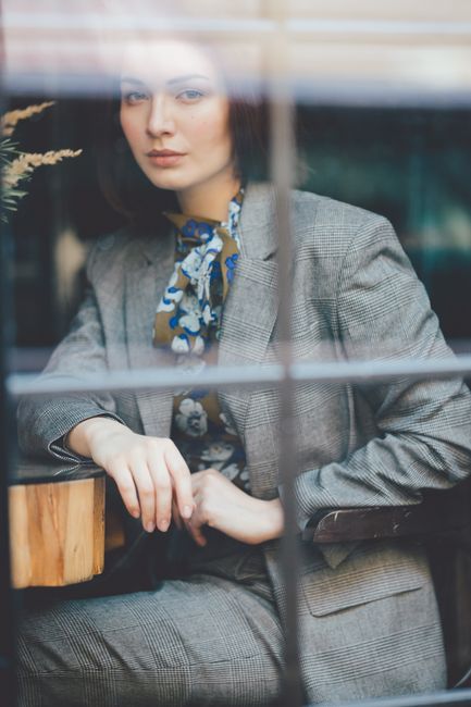 Through fenced window view of young female in gray suit sitting in armchair while looking at camera in building