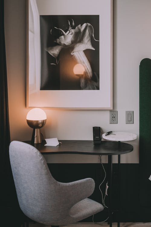 Soft armchair against table with shiny lamp reflecting in photography on wall in house