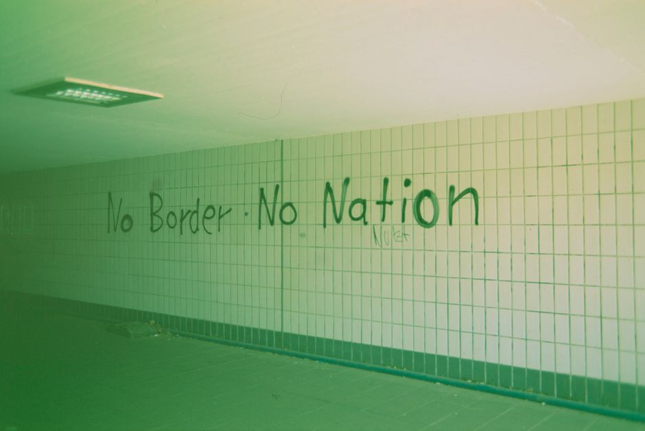 Wall with 'No Border No Nation' graffiti in an urban tunnel, highlighting political sentiment.
