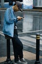 一名男子穿着休闲街头服饰，在下雨的街道上靠在护柱上使用手机