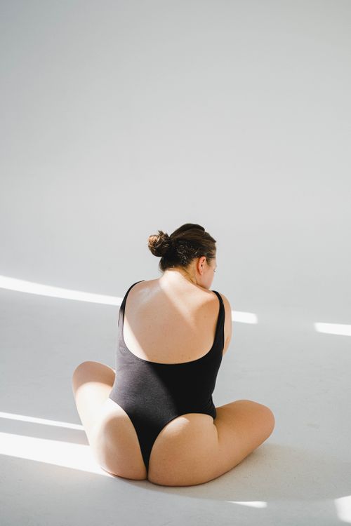 Free Elegantly lit image of a woman in a black bodysuit sitting indoors with natural sunlight. Stock Photo