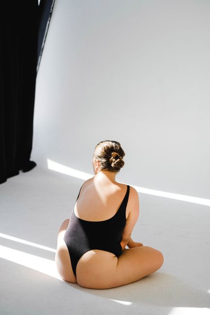 Back view of a woman wearing a black bodysuit in bright studio lighting, showcasing elegant fashion.