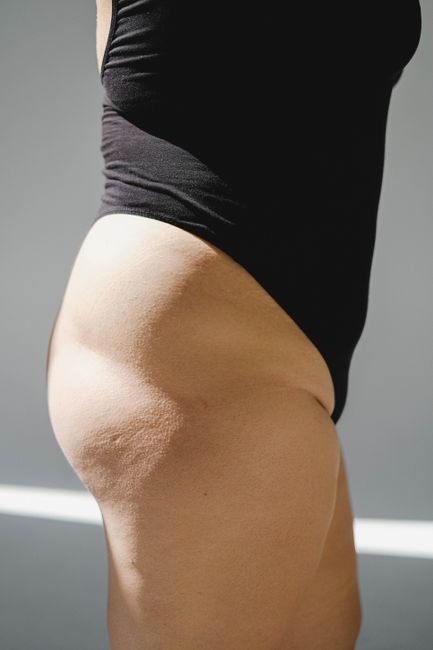 A close-up of a woman's legs and hips wearing black swimwear in natural lighting indoors.