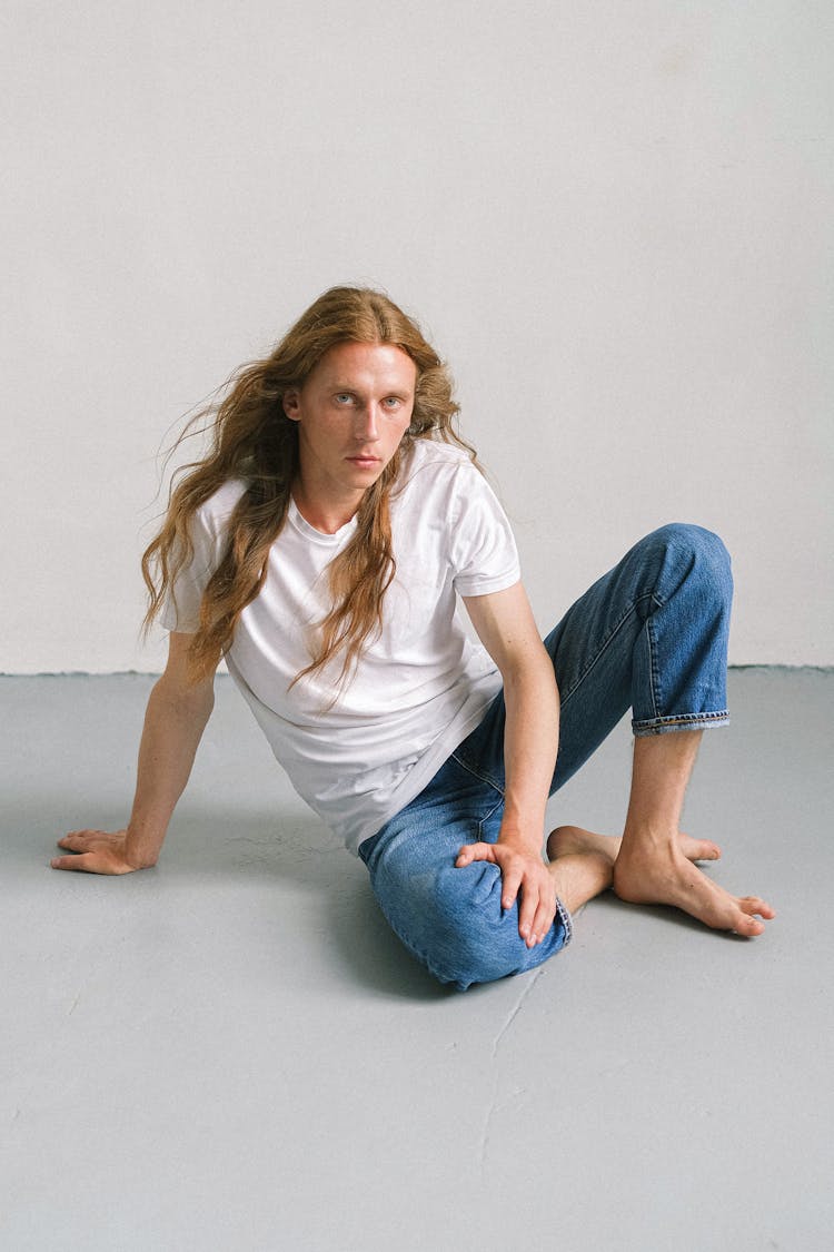 Emotionless Androgynous Man Sitting On Floor In Studio