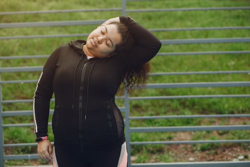 Free Woman in sportswear stretching outdoors with closed eyes and peaceful expression. Stock Photo