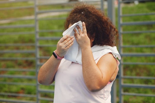 Woman wipes sweat after outdoor workout in summer sun, showing fitness and resilience.