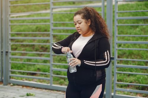 Free A woman in sportswear prepares for exercise, opening a water bottle outdoors. Stock Photo