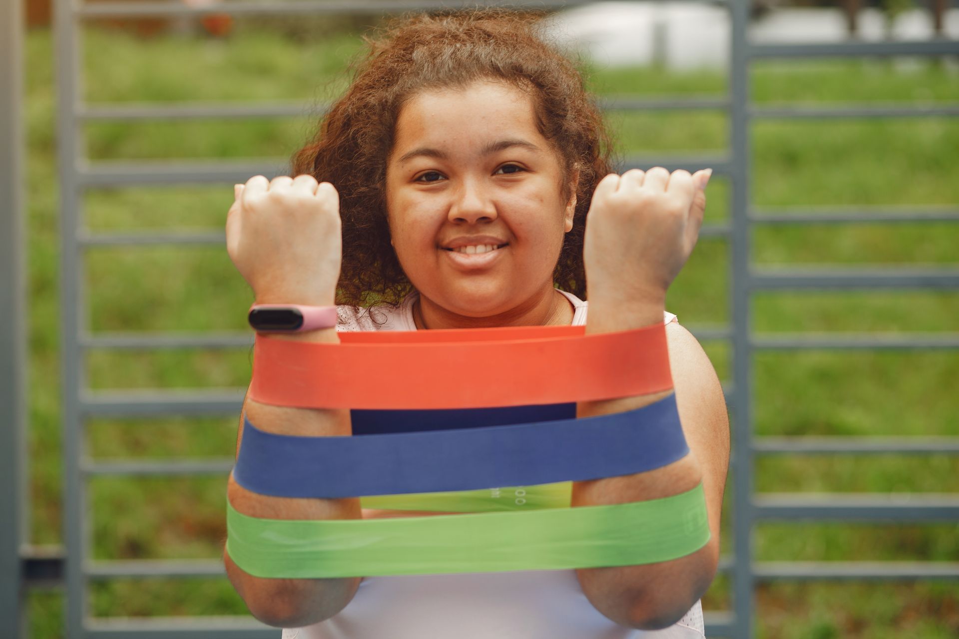 Smiling woman exercising with colorful resistance bands outdoors, promoting fitness and joy.