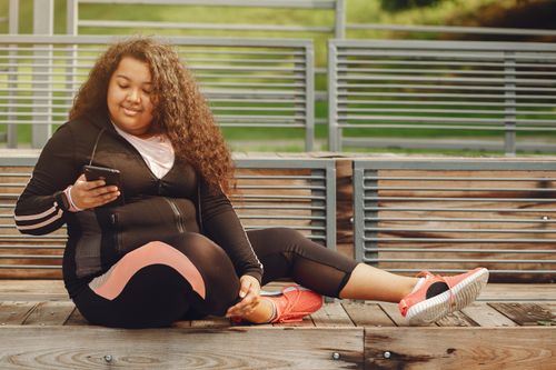 Free Woman in sportswear relaxing outdoors while using a smartphone, enjoying a sunny day. Stock Photo