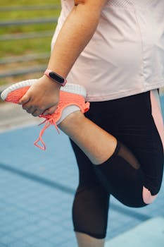 Close-up of a woman stretching her leg while wearing fitness attire outdoors.
