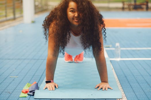 Woman with curly hair doing plank exercise on a yoga mat outdoors, smiling and enjoying a sunny day.
