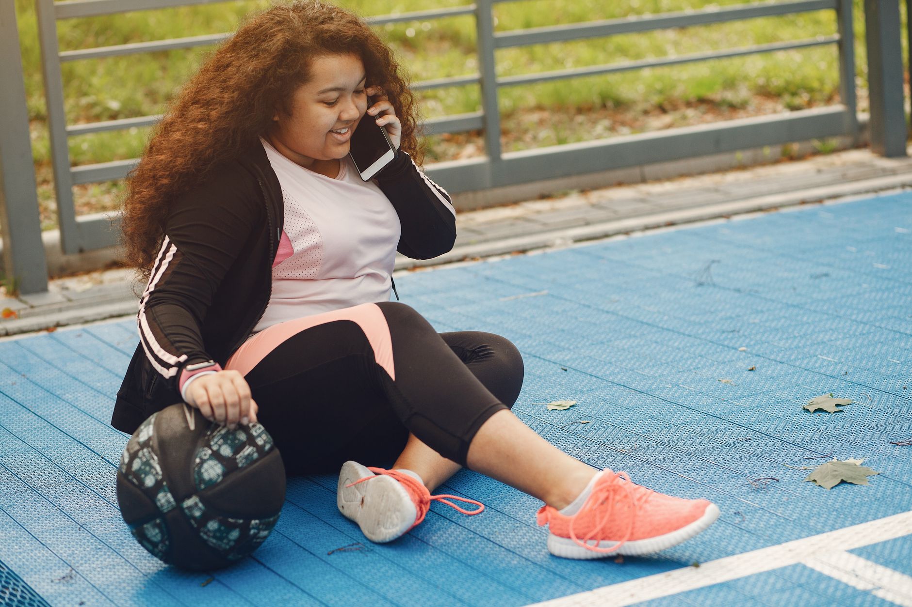 Smiling woman multitasks exercise and phone call on outdoor track.