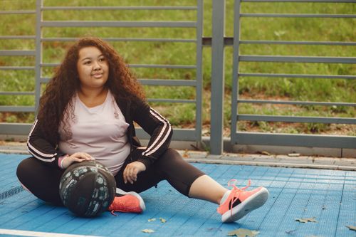 Free A woman enjoys a moment of relaxation sitting on an outdoor basketball court with a ball. Stock Photo