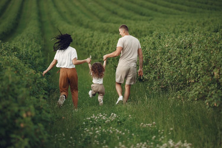 Happy Parents With Child Running On Green Field