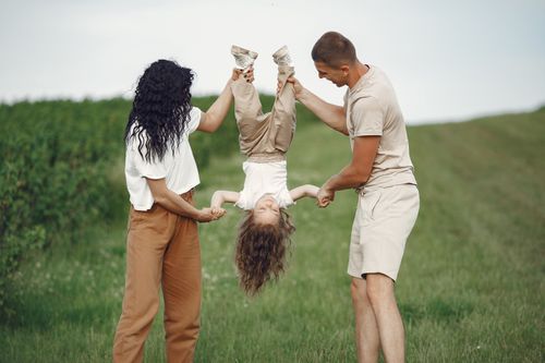 Free A joyful family enjoys outdoor play, lifting their child upside down in a green field. Stock Photo