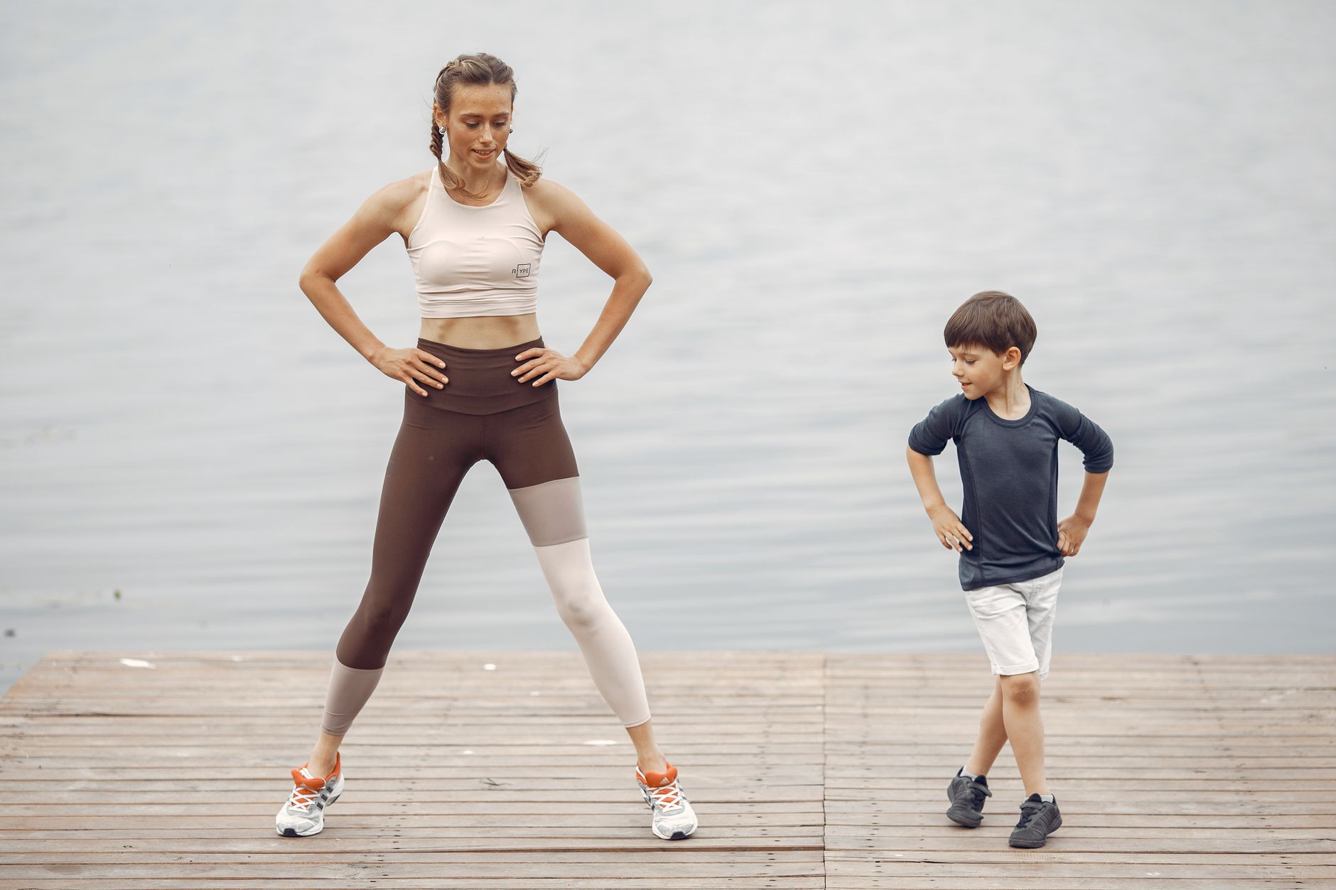 A mother and son exercising together on a wooden pier by the lake, enjoying fitness and fun.