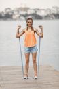 一名穿着运动服的女子在湖边码头上用阻力带锻炼