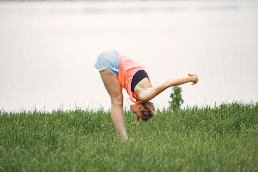 A woman in sports clothing practicing yoga and stretching in a grassy field.