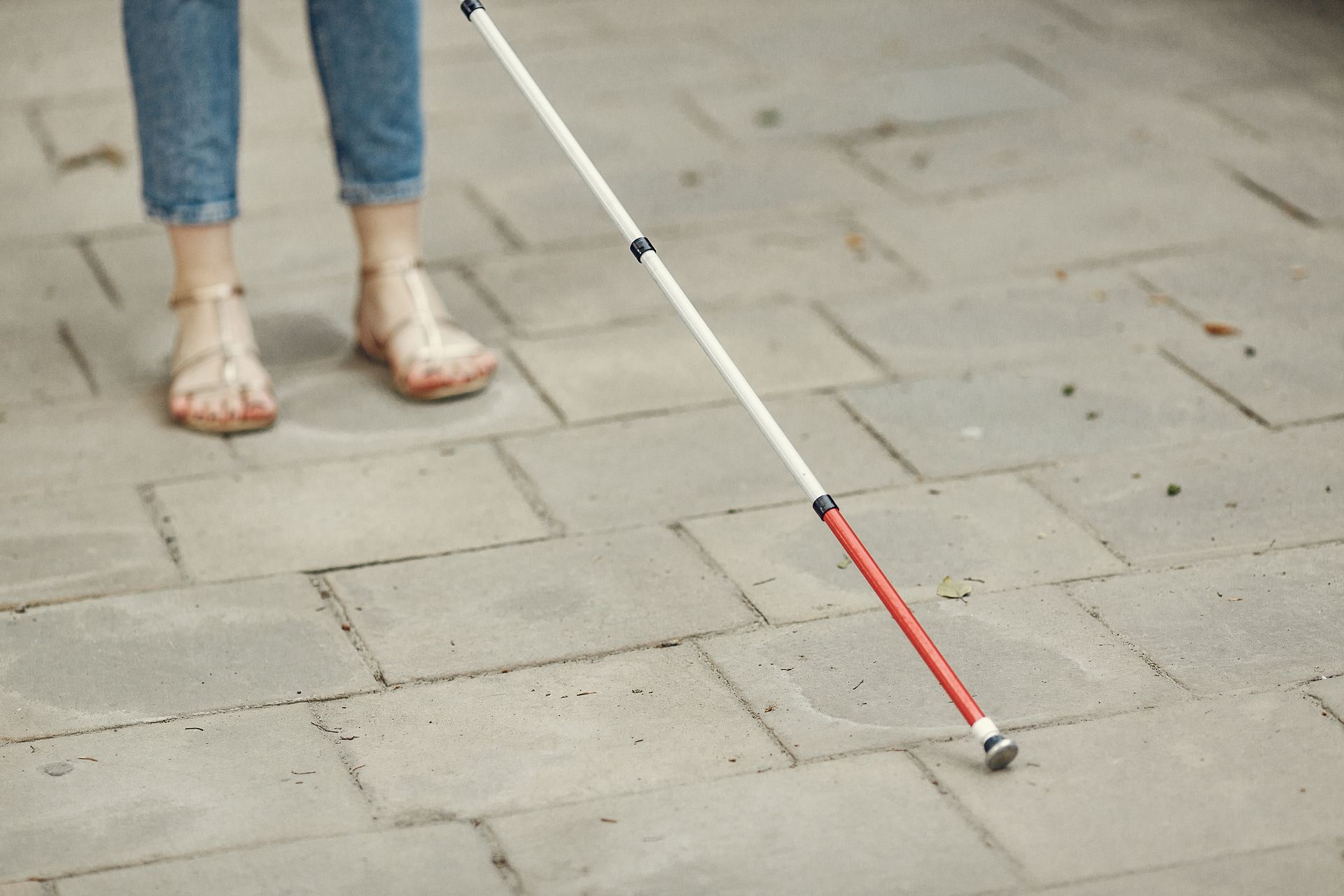 Close-up of legs and cane, depicting mobility aid use on a paved sidewalk.