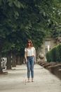 Woman in White Long Sleeve Shirt and Blue Denim Jeans Standing on Gray Concrete Pathway during