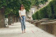 Woman in White Shirt and Blue Denim Jeans Standing on Sidewalk