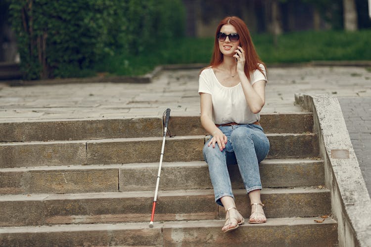 Blind Woman Sitting On The Concrete Stairs While Making A Phone Call