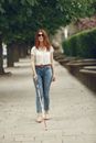 Woman in White Tank Top and Blue Denim Jeans Standing on Gray Concrete Pathway