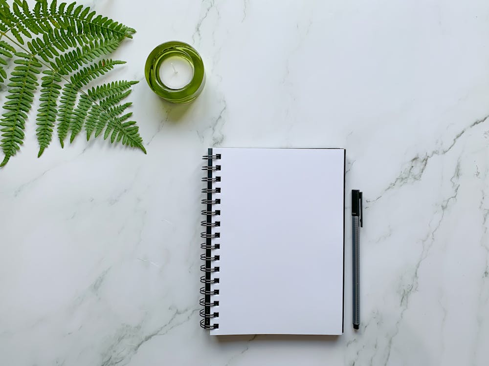 White Spiral Notebook Beside Green Ceramic Mug