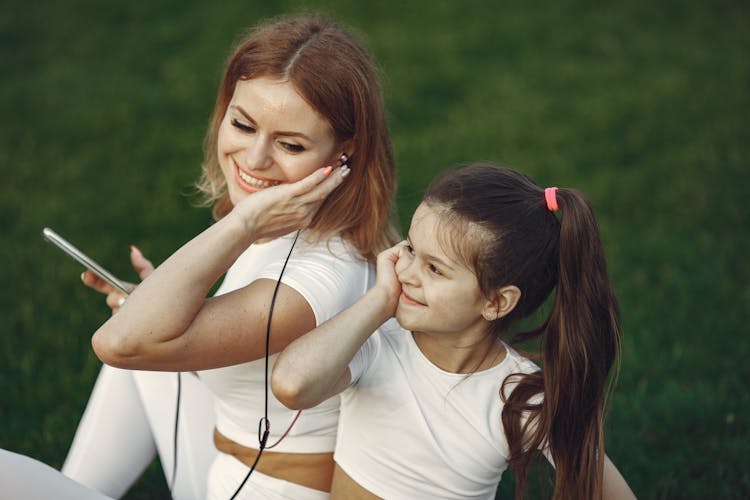 A Woman Sharing Earphones With Her Daughter