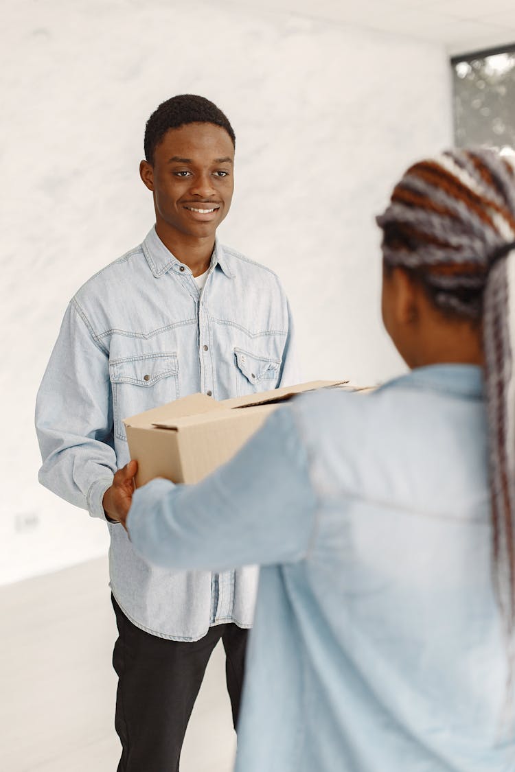 A Person Handing A Cardboard Box To A Man