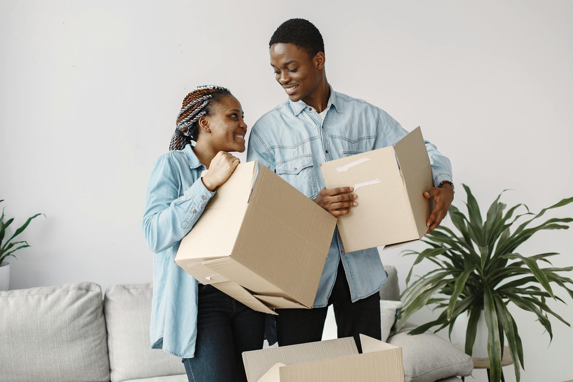 A smiling couple carrying cardboard boxes while moving indoors, capturing a joyful moment.