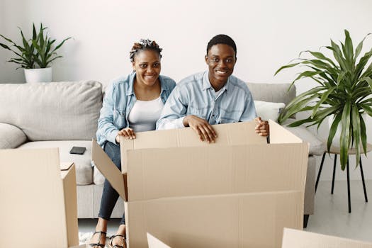 A young couple smiling while unpacking boxes in their living room, creating a joyful moving experience.