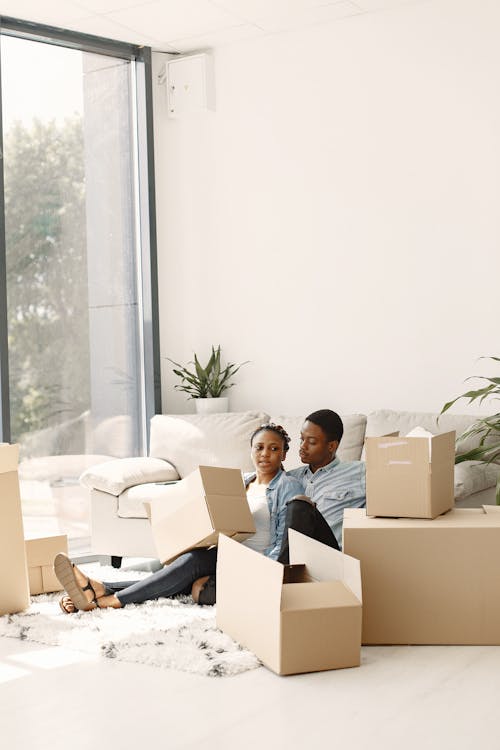 Free A Young Couple Sitting in a Living Room Full of Cardboard Boxes Stock Photo