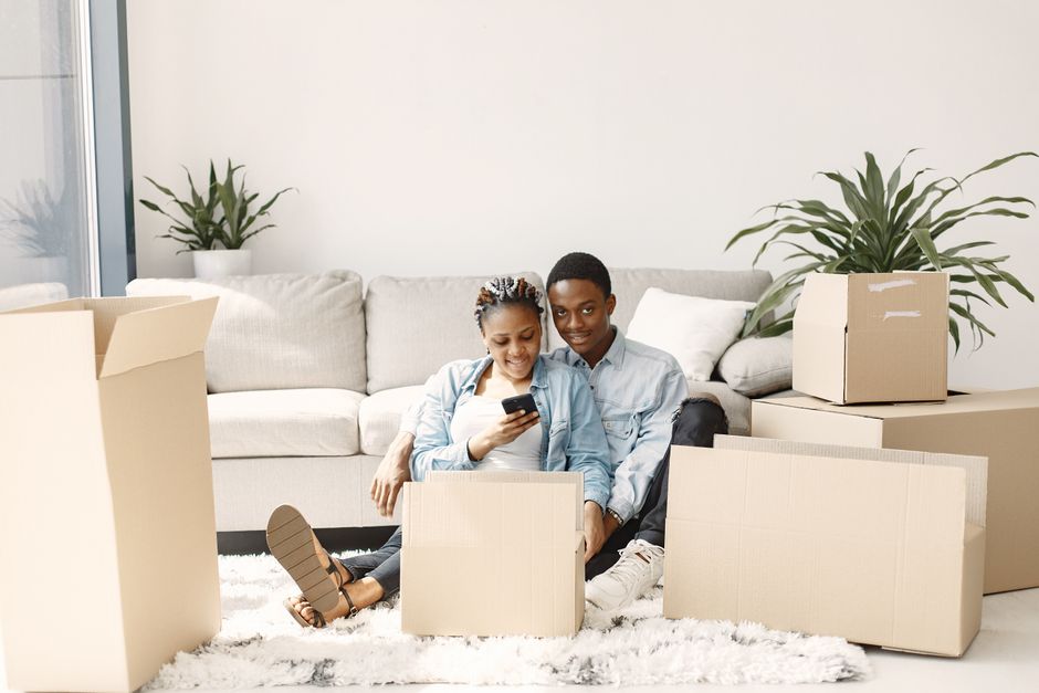 Group of young Black Nigerian friends in a Birmingham living room unpacking a shared bulk grocery order, sorting containers of palm oil and other Nigerian food staples into separate piles on the floor, warm evening light, photorealistic
