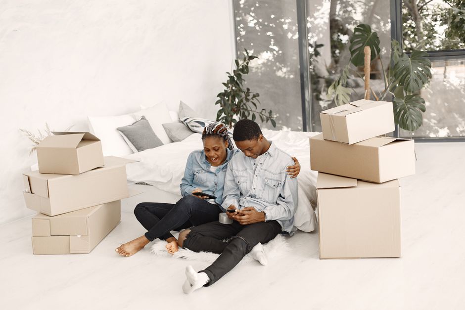 Group of young Black Nigerian and West African friends in a Manchester living room sorting shared bags of groceries including yam tubers and palm oil into separate piles, warm evening light, photorealistic