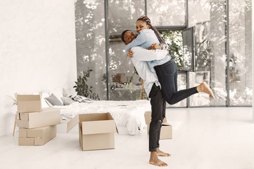 Free Joyful couple embracing in their new home surrounded by moving boxes, reflecting excitement and togetherness. Stock Photo