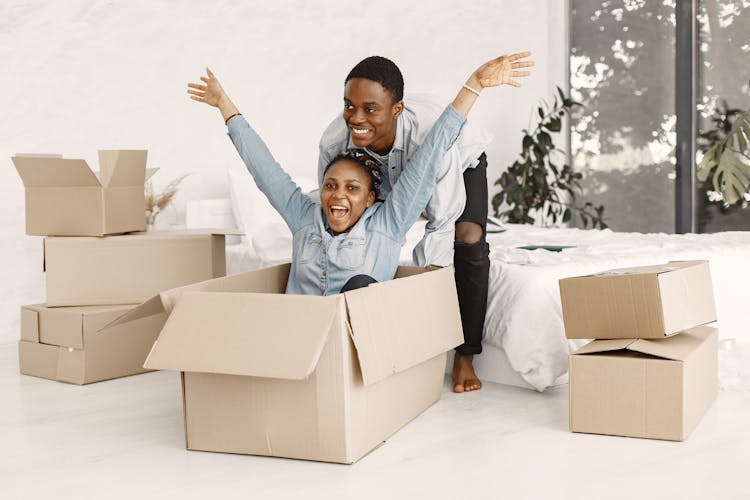 A Man Pushing A Happy Woman Sitting In A Cardboard Box