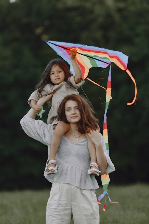 A Little Girl Holding a Kite while Sitting on her Mother's Shoulders