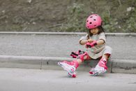 A Little Girl in Rollerblades Sitting on a Curb