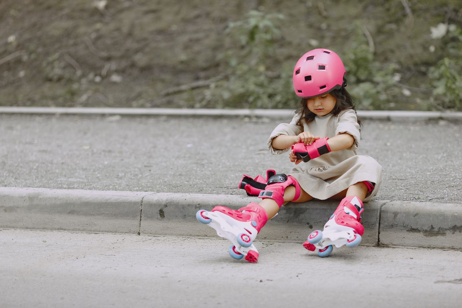Young girl in a pink helmet and rollerblades adjusts her safety gear before skating