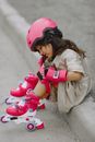 A Little Girl in Rollerblades Sitting on a Curb