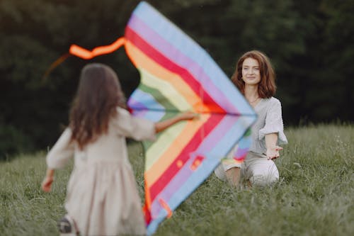 Free Girl in White Long Sleeve Shirt Holding Multi Colored Flag Standing on Green Grass Field during Stock Photo