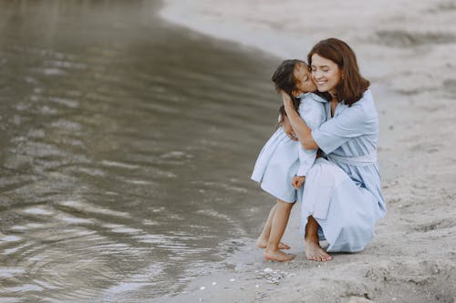 Free A Little Girl Kissing her Mom by the Shore Stock Photo