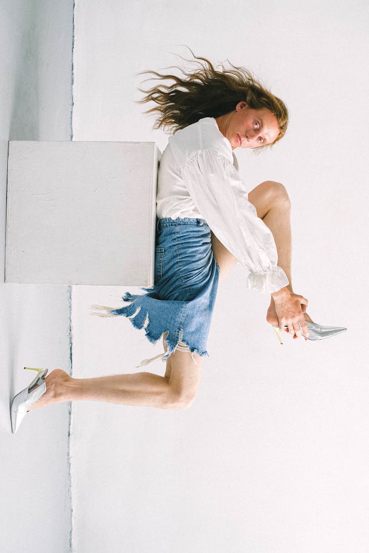 Serious Young Gender Fluid Man Wearing Shoes While Lying On White Cube