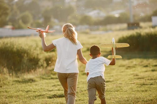 Back View of Woman and a Boy Playing with Plane Models on a Green Field