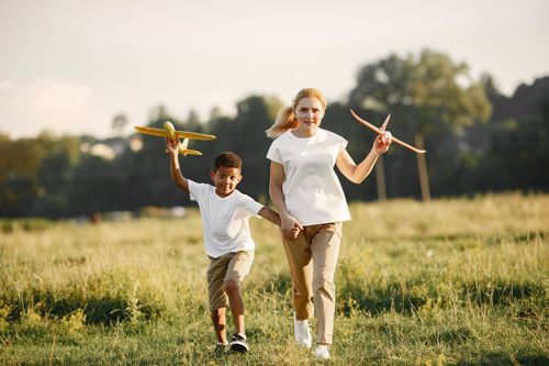 Free A joyful mother and son running and playing with toy planes in a sunny park. Stock Photo