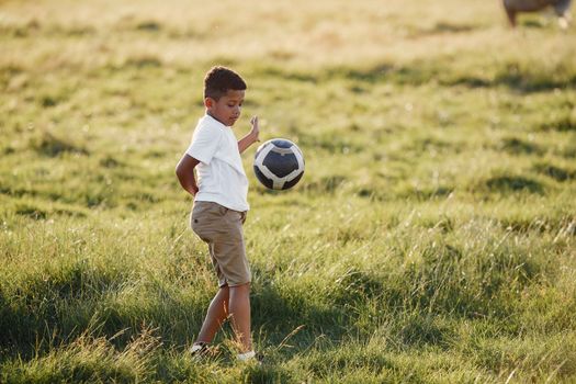 A young boy enjoying soccer in a sunlit meadow during a summer day, showcasing active outdoor fun.